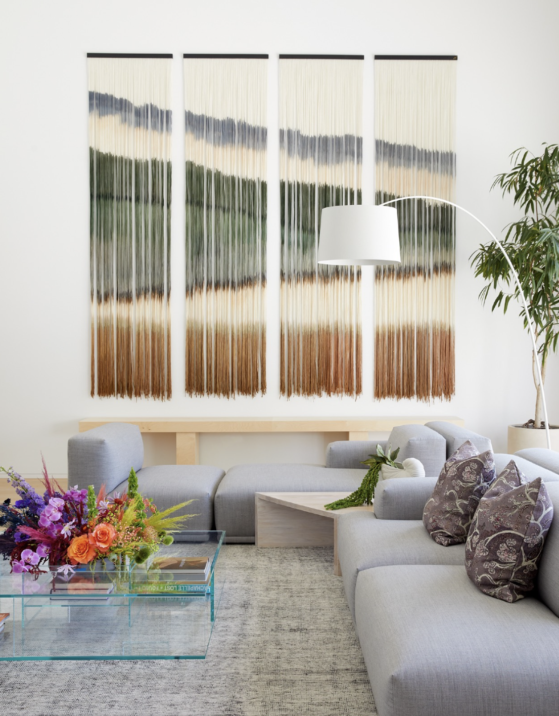 Living room with sectional sofa, textile wall hanging, glass table, and flowers