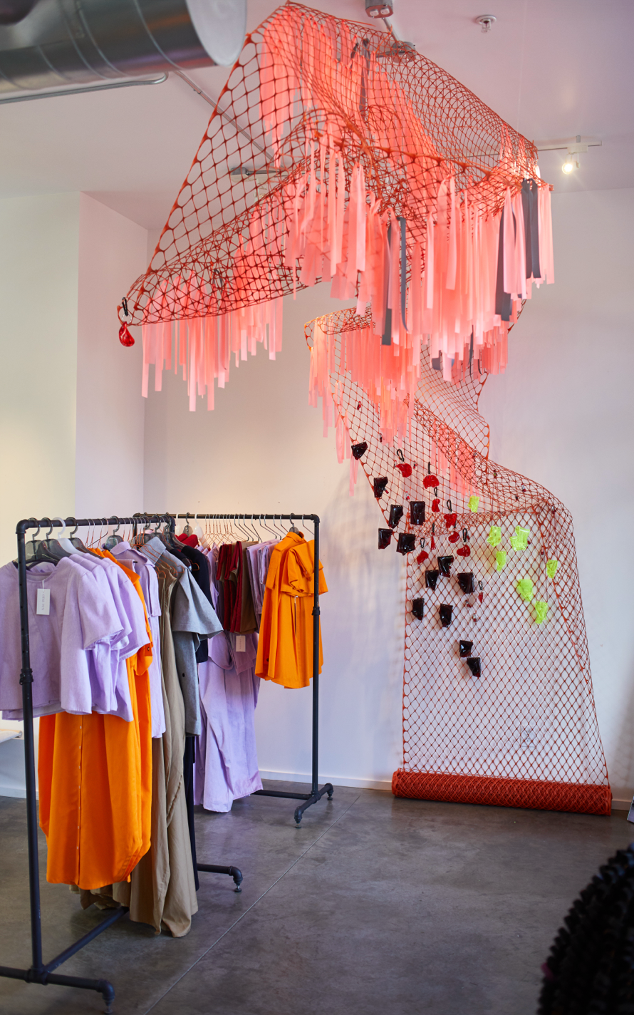 Retail installation with suspended red netting and colorful garments